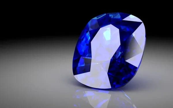 A single deep blue cushion-cut sapphire photographed against a dark graduated studio background