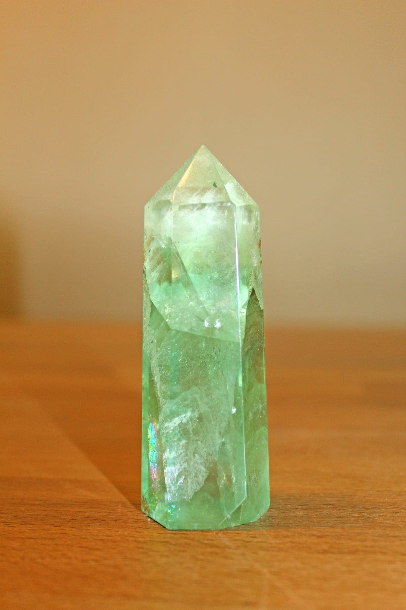 A polished pale green crystal point standing upright on a wooden surface