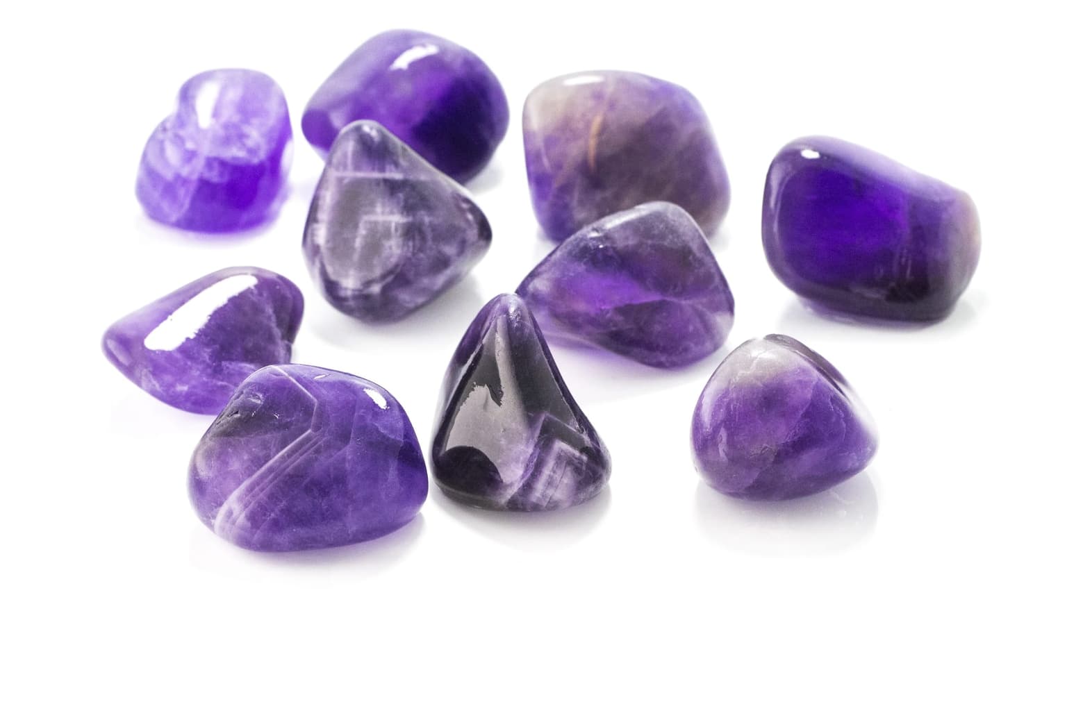 Several tumbled and polished purple amethyst stones grouped on a white background